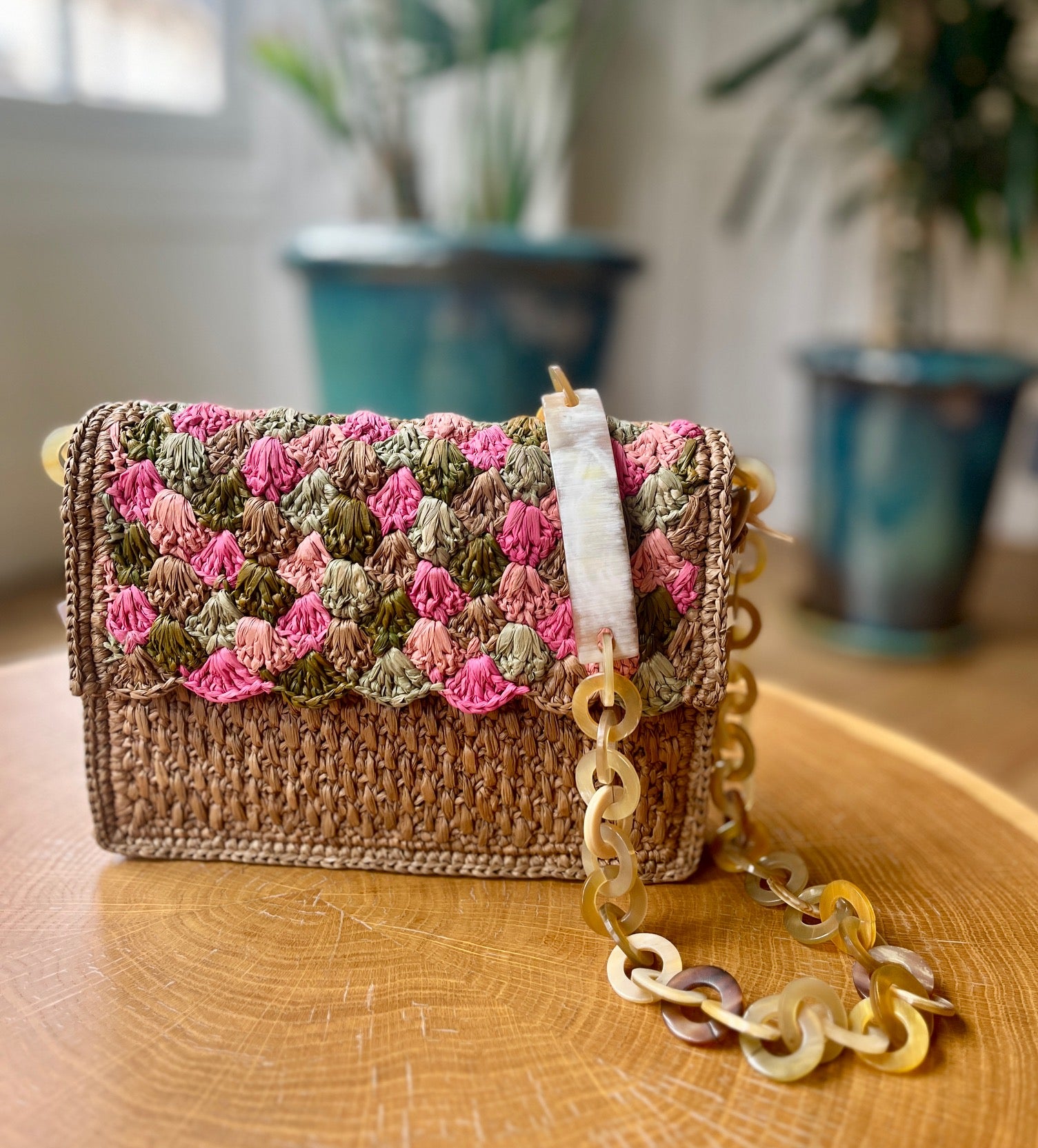 Sac artisanal en raphia kaki et rose, orné d'une chaîne en corne, parfait pour compléter une tenue chic et décontractée.