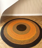 Tapis artisanal rond en raphia avec des couleurs naturelles orange, brun et noir, diamètre 200 cm, conçu à Madagascar.
