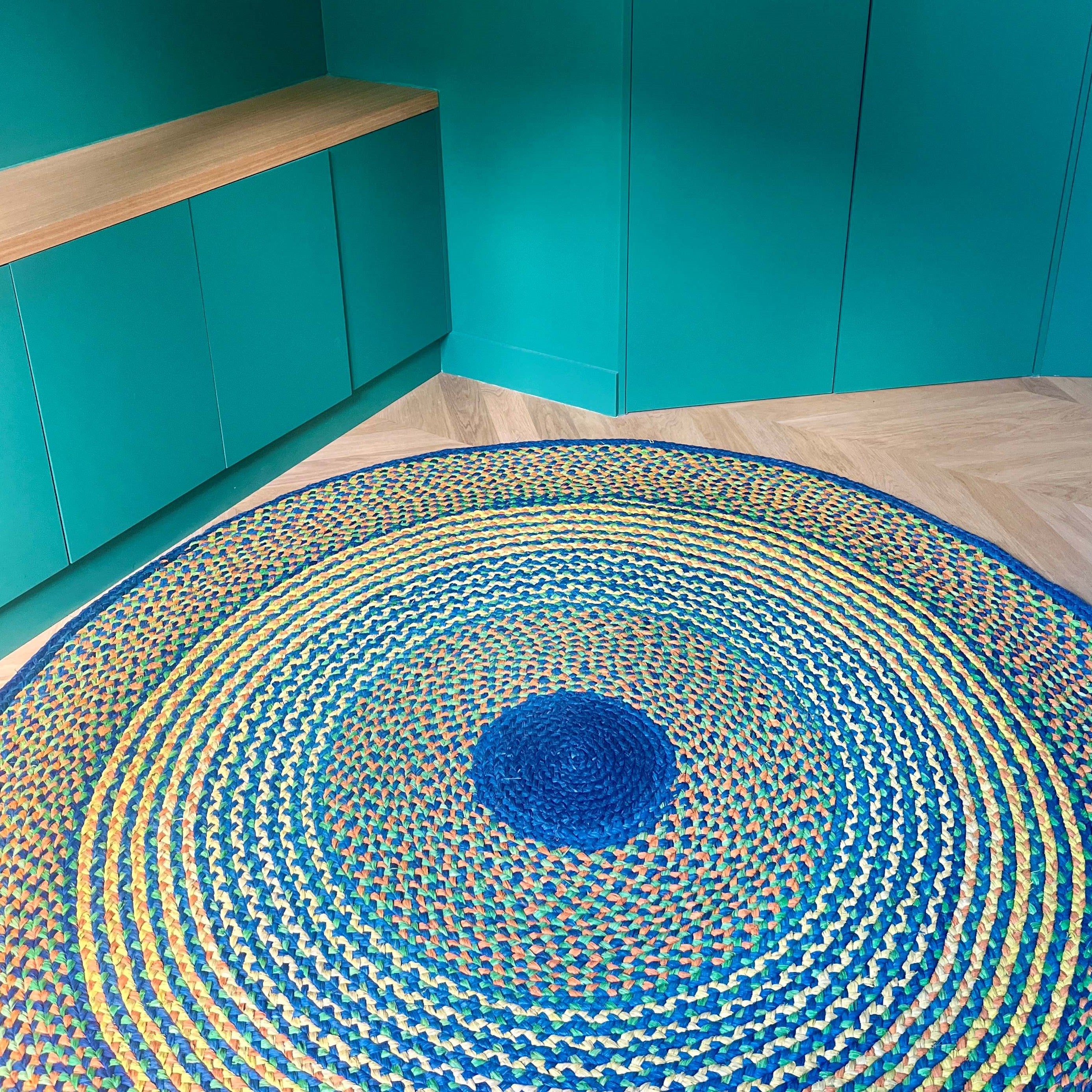 Tapis rond en raphia aux nuances jaune, bleu, turquoise et vert émeraude, fait main à Madagascar, diamètre 200 cm.