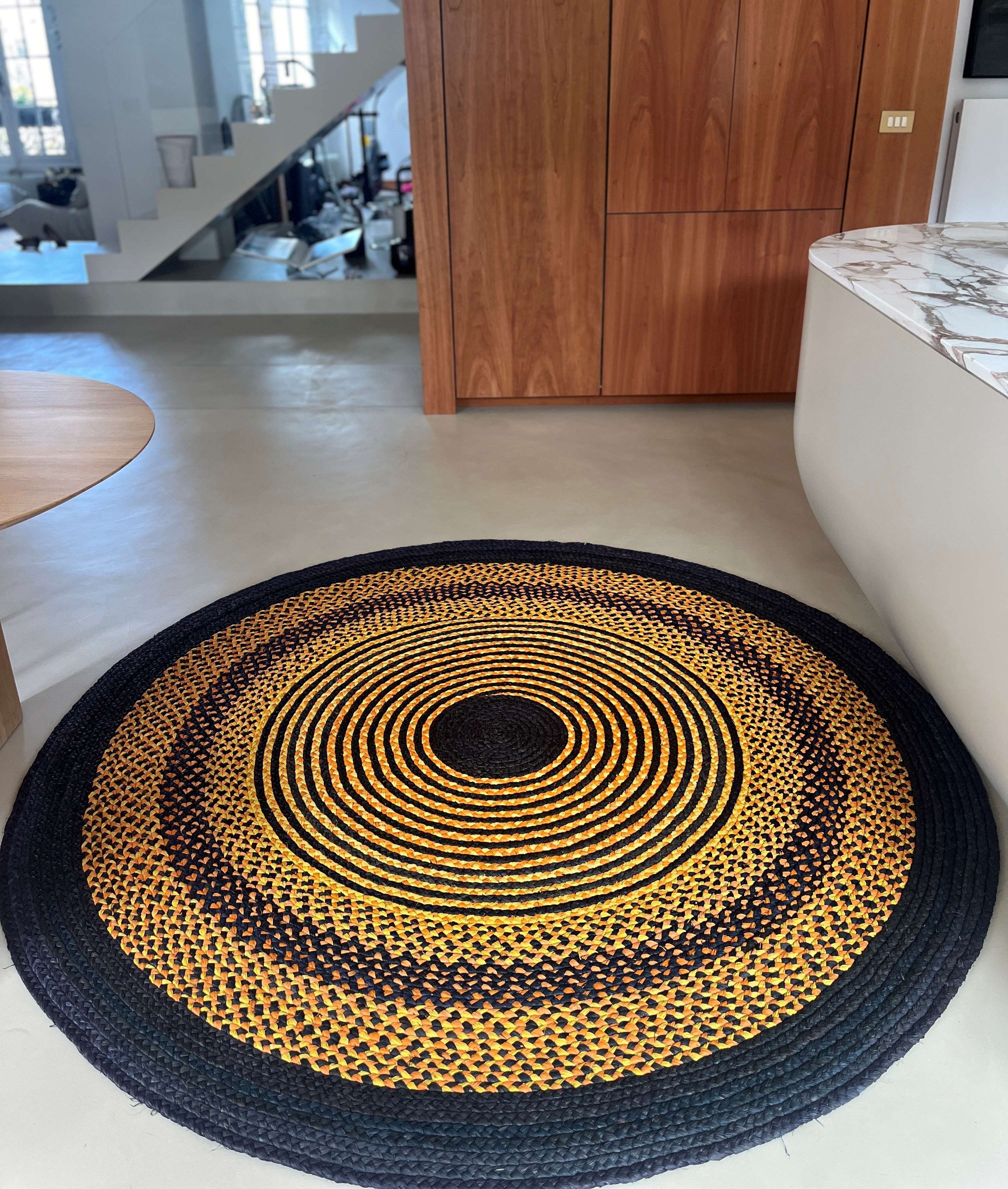 Tapis rond unique en raphia, aux tons noir, jaune et terracotta, 200 cm de diamètre, fait main à Madagascar.